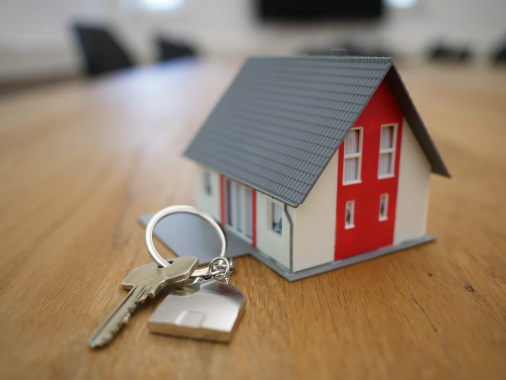 Miniatura de casa e chaves sobre mesa, representando construção com financiamento